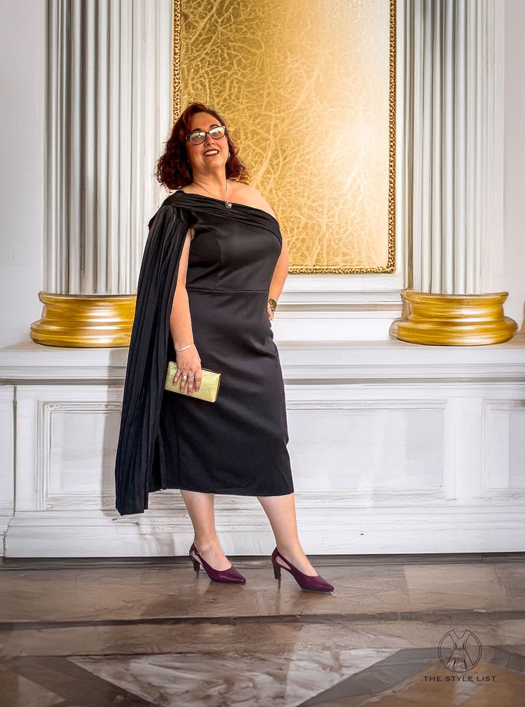 A woman in a black dress is standing in front of a wall.
