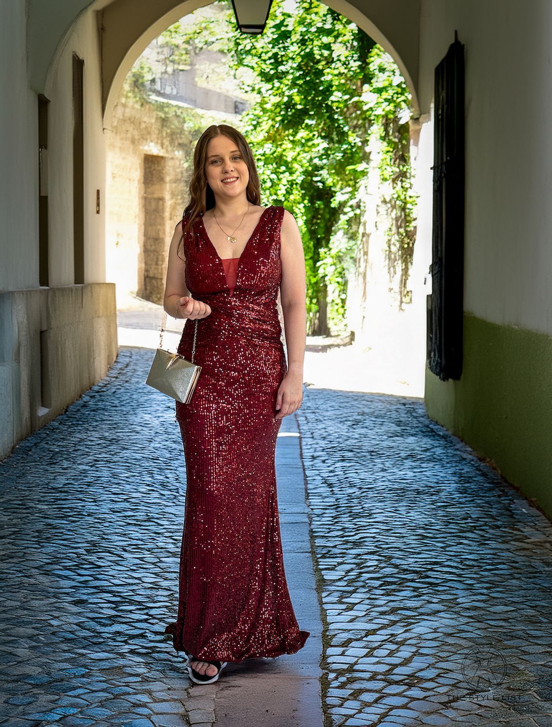 A woman in a red sequined dress is walking down a cobblestone street.