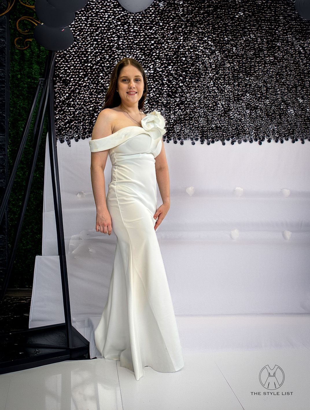 A woman in a white dress is standing in front of a black wall.