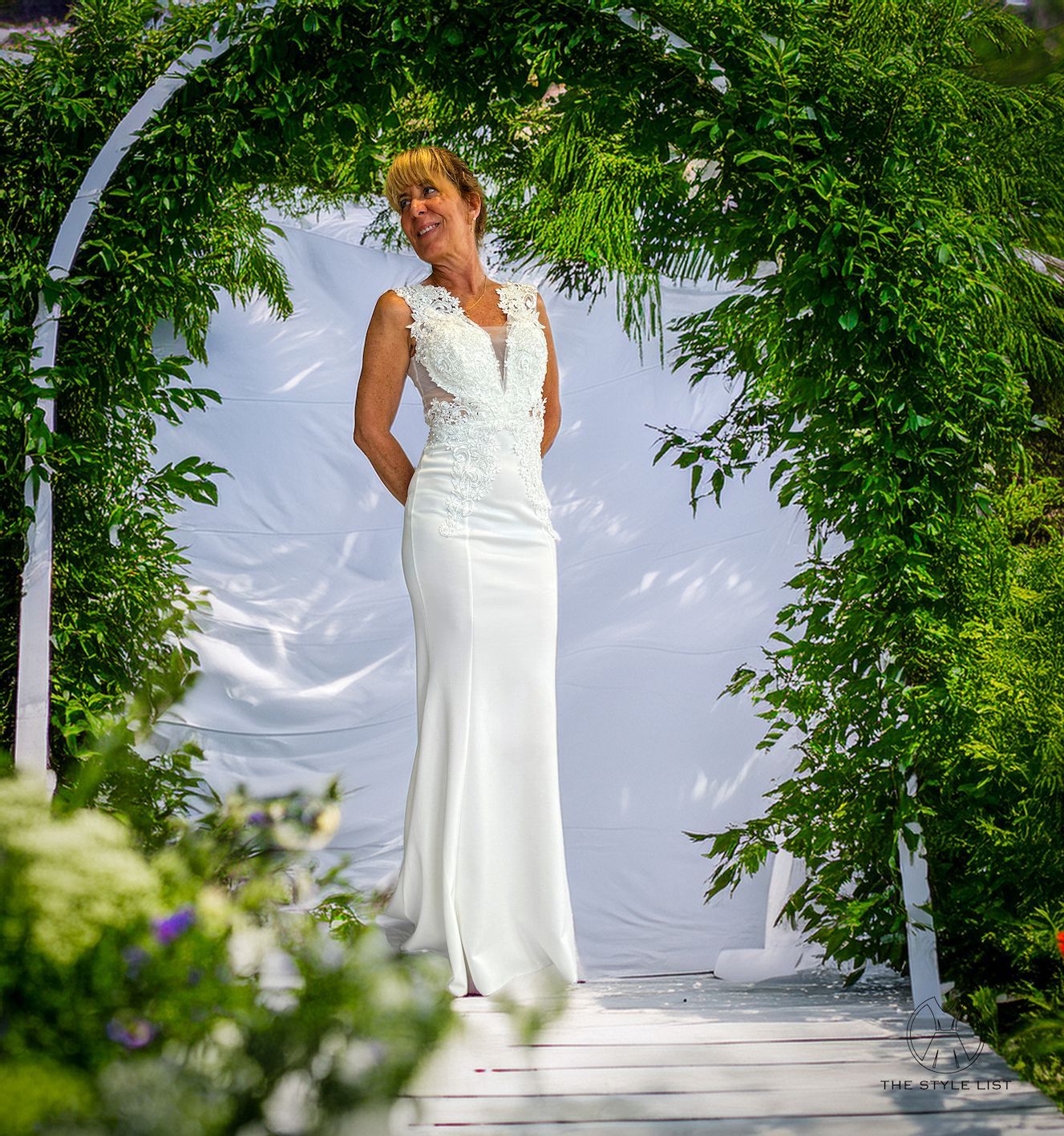 A woman in a white dress is standing under a green archway.