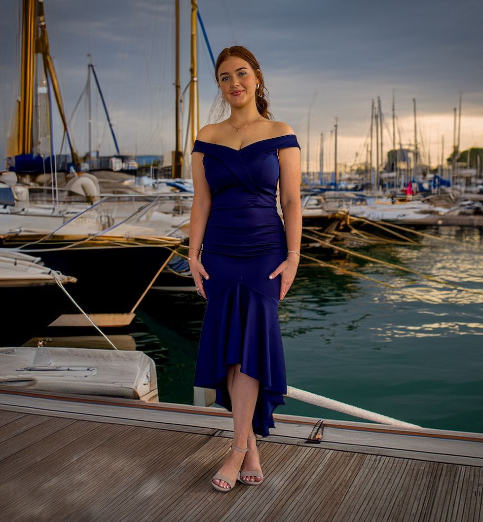 A woman in a blue dress is standing on a dock in front of boats.