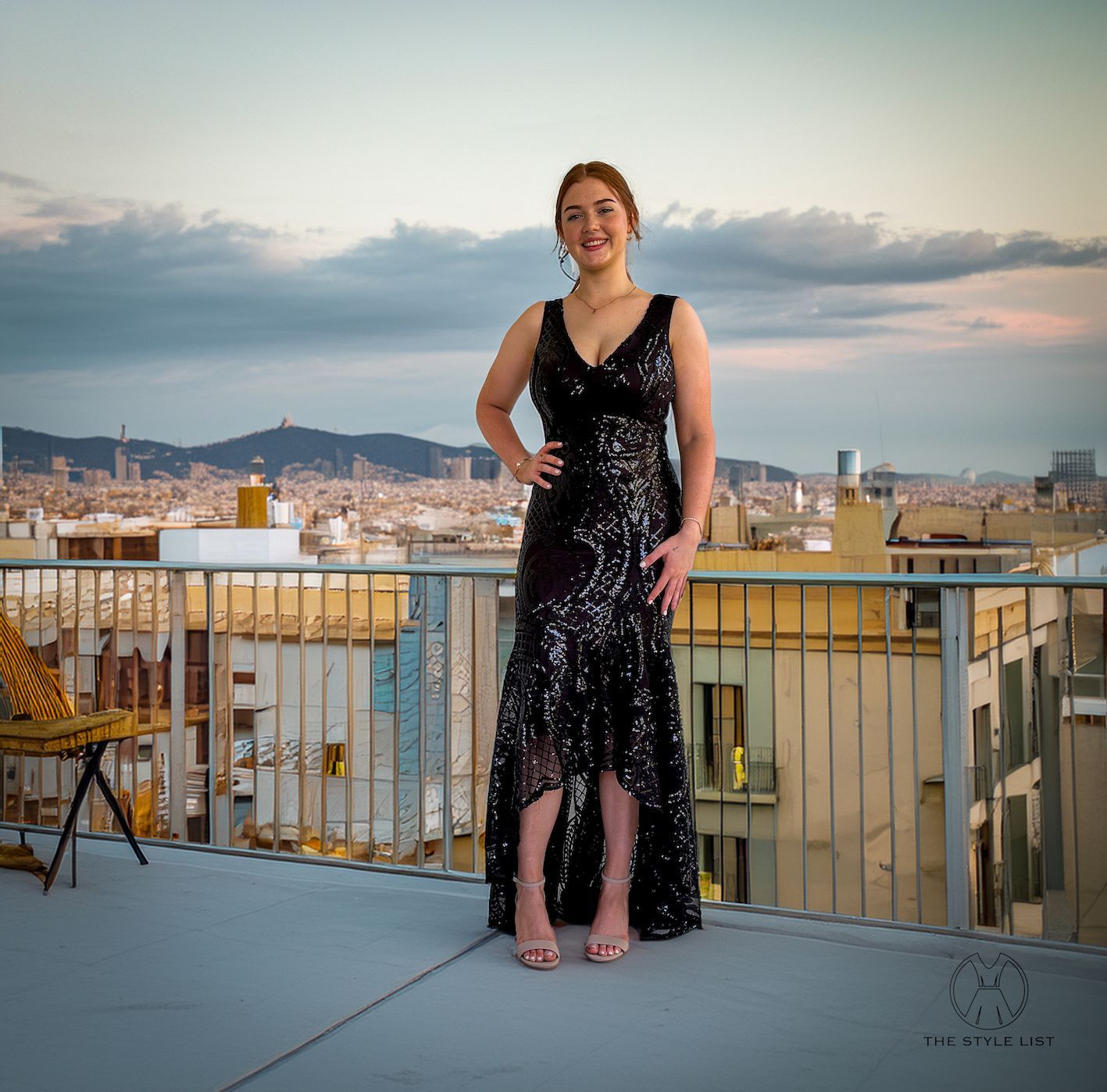 A woman in a black dress stands on a balcony overlooking a city