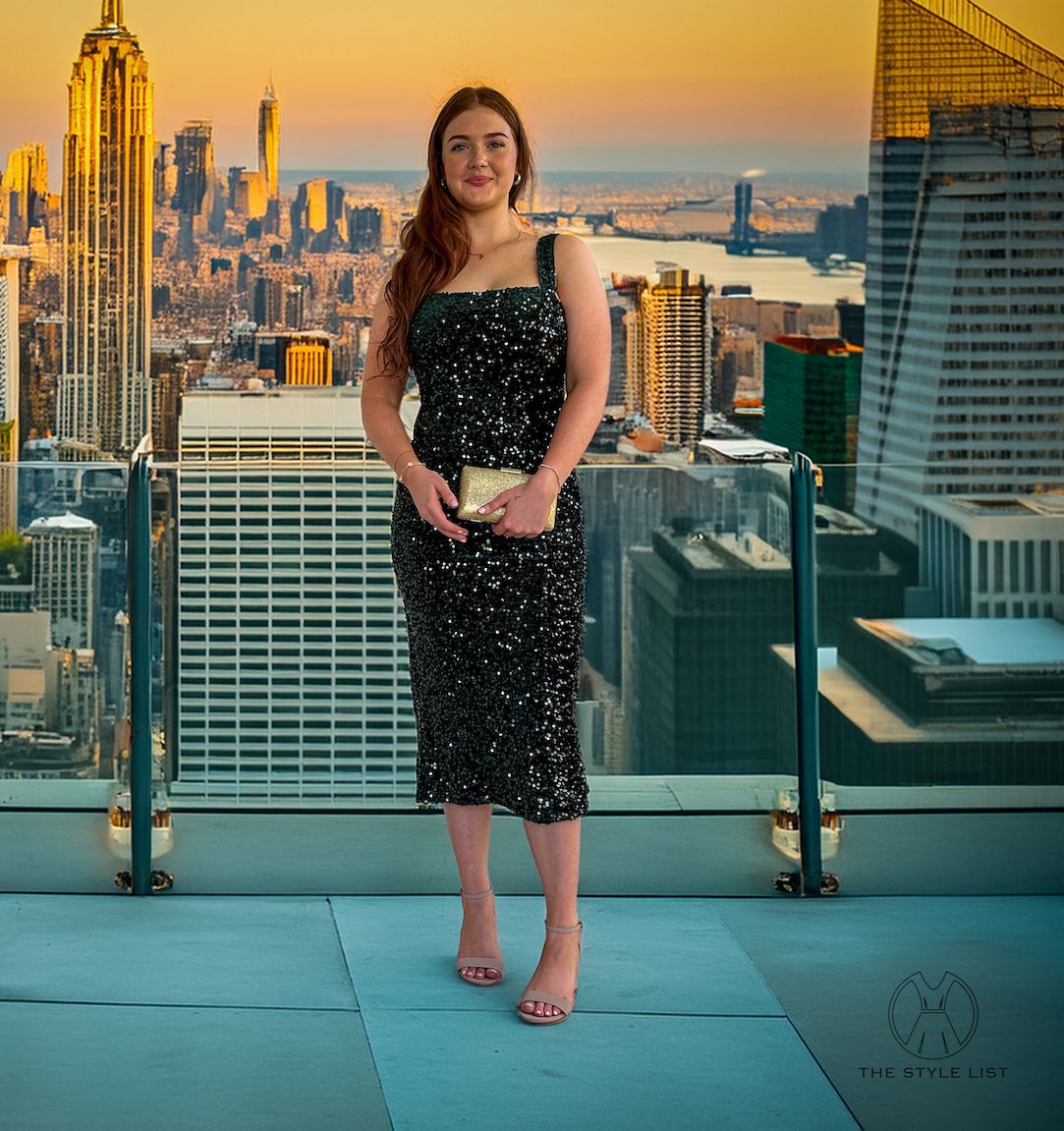 A woman in a black dress is standing on a balcony overlooking a city