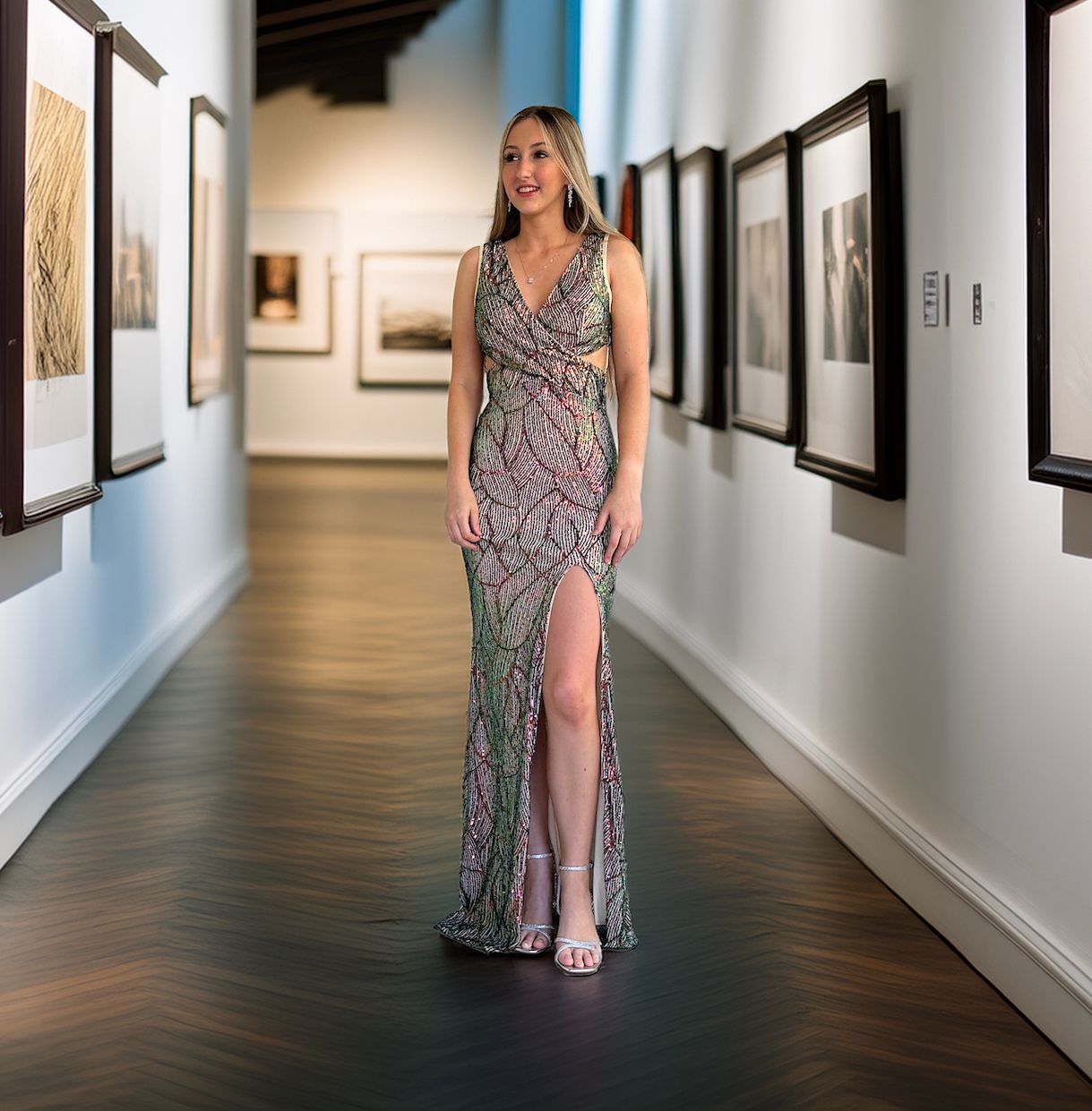A woman in a long dress is standing in a hallway with pictures on the wall.
