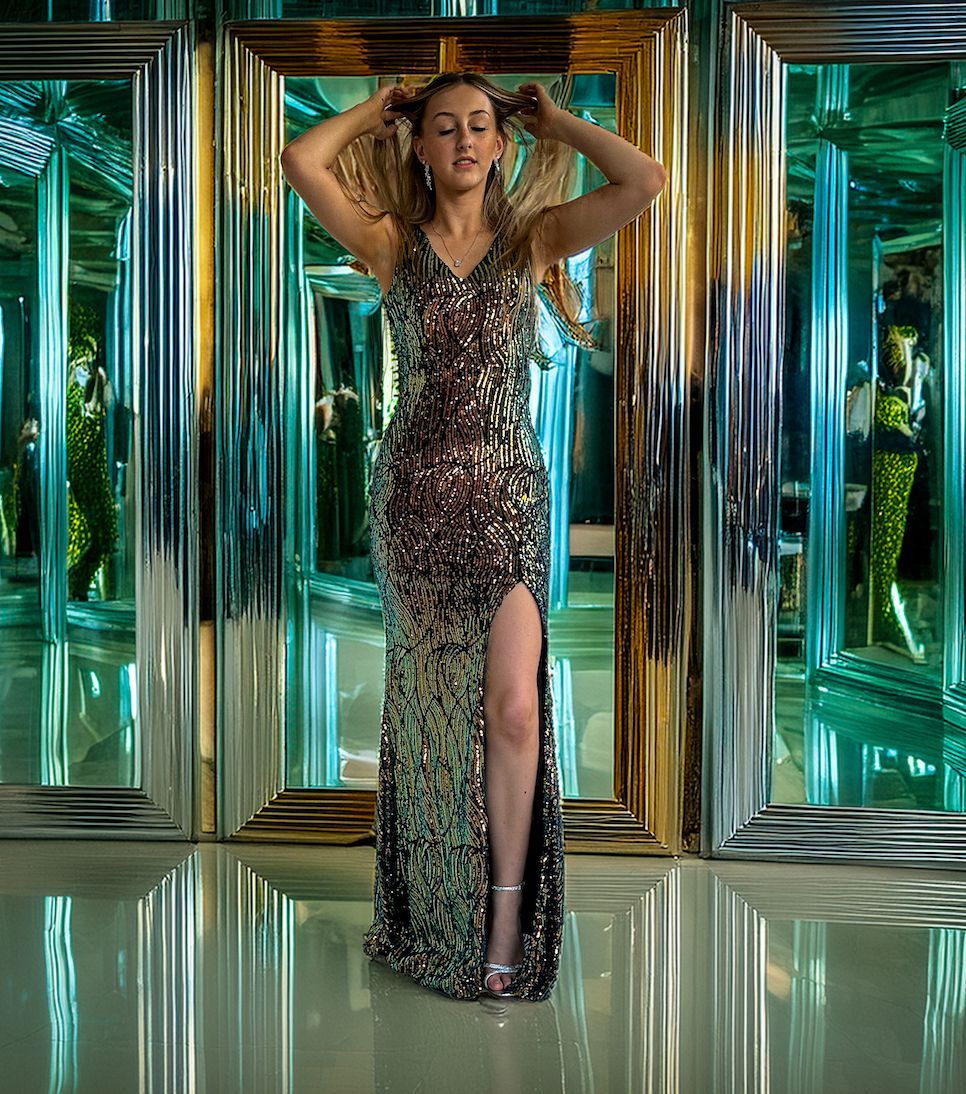 A woman in a long dress is standing in front of a mirror.