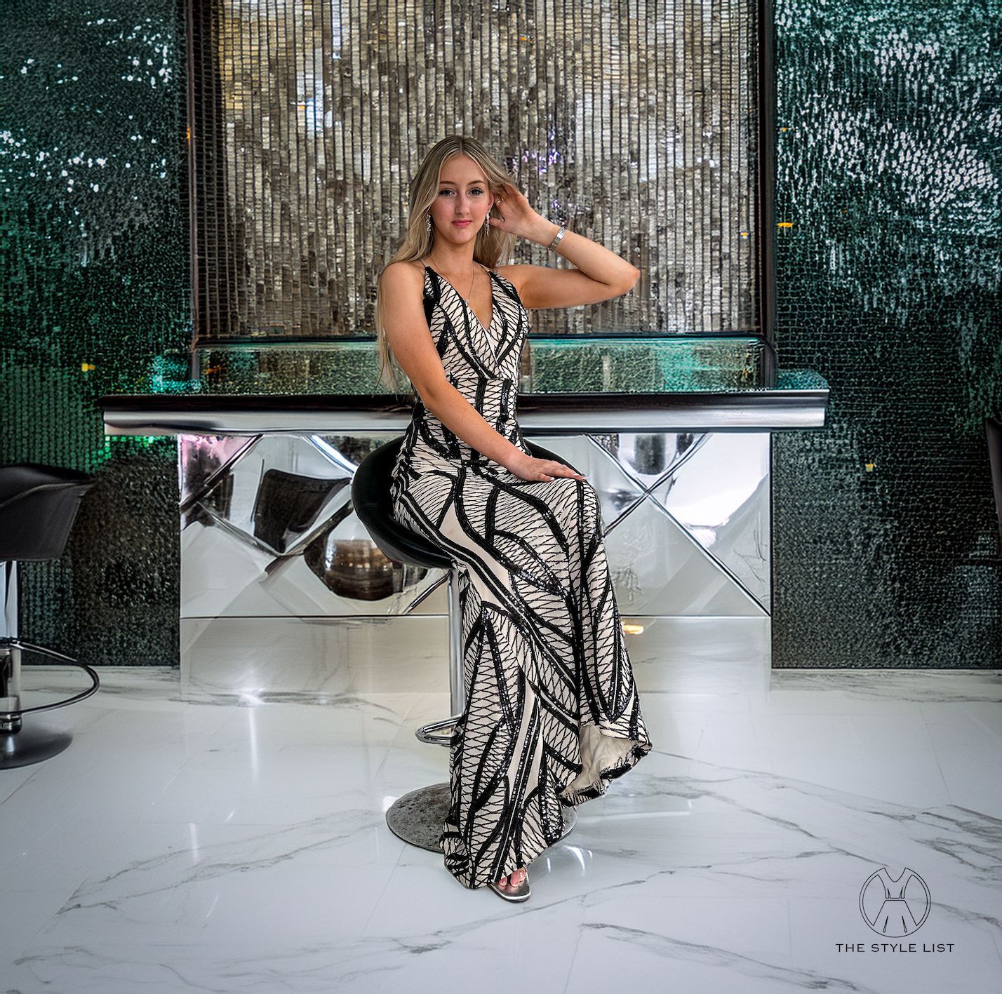 A woman in a black and white dress is sitting on a bar stool