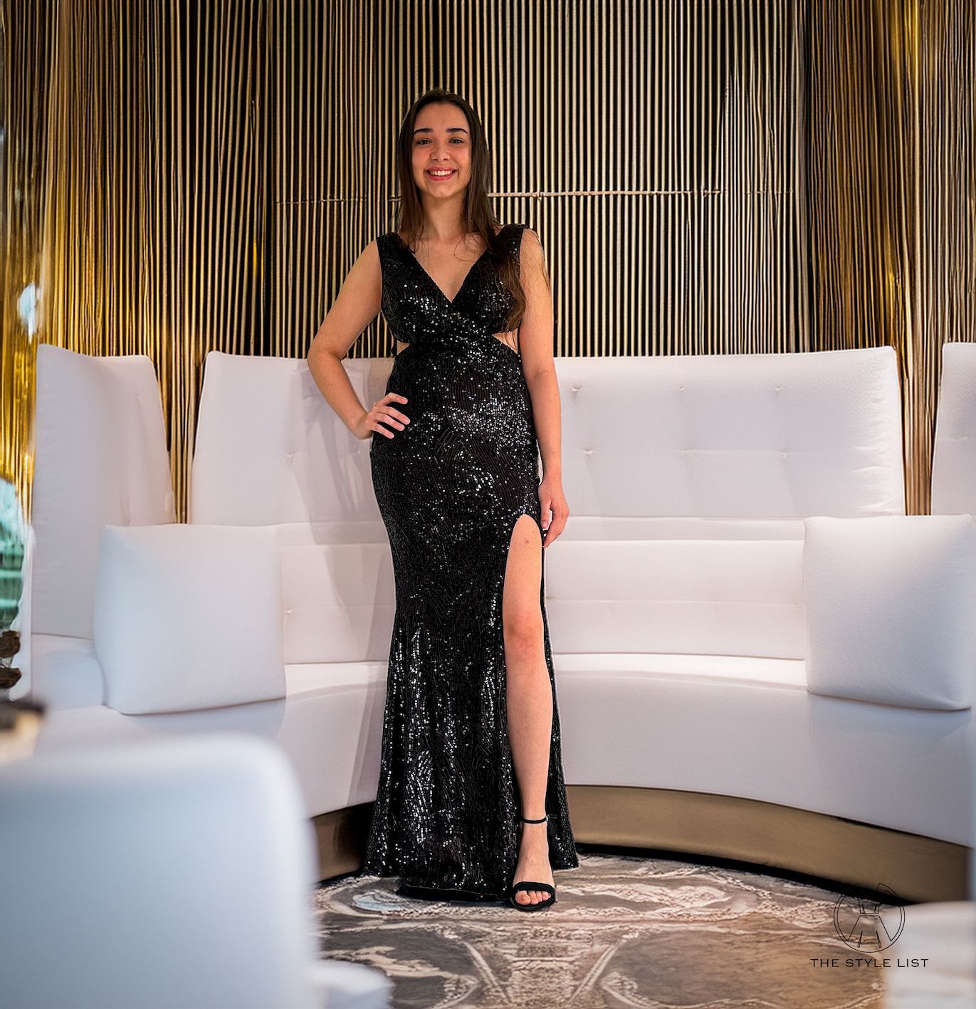 A woman in a black sequined dress is standing next to a white couch.