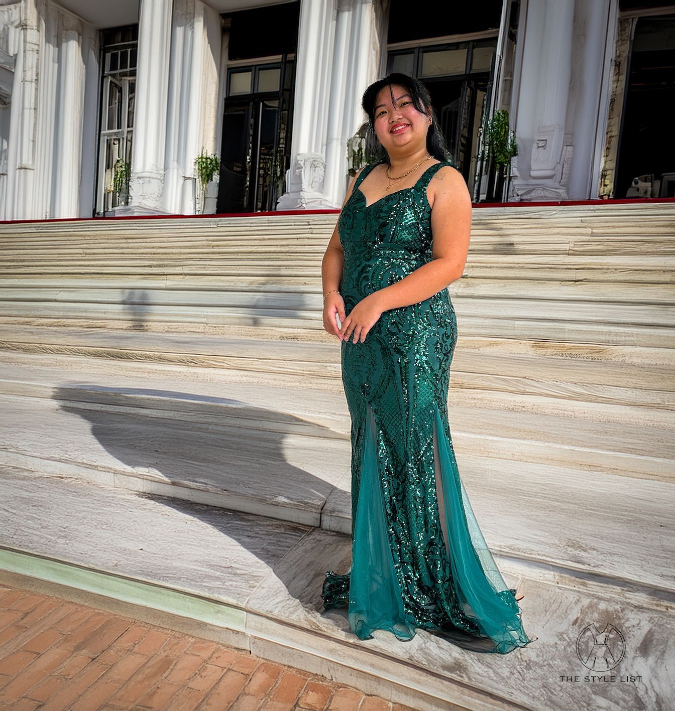 A woman in a green sequined dress is standing in front of a building.