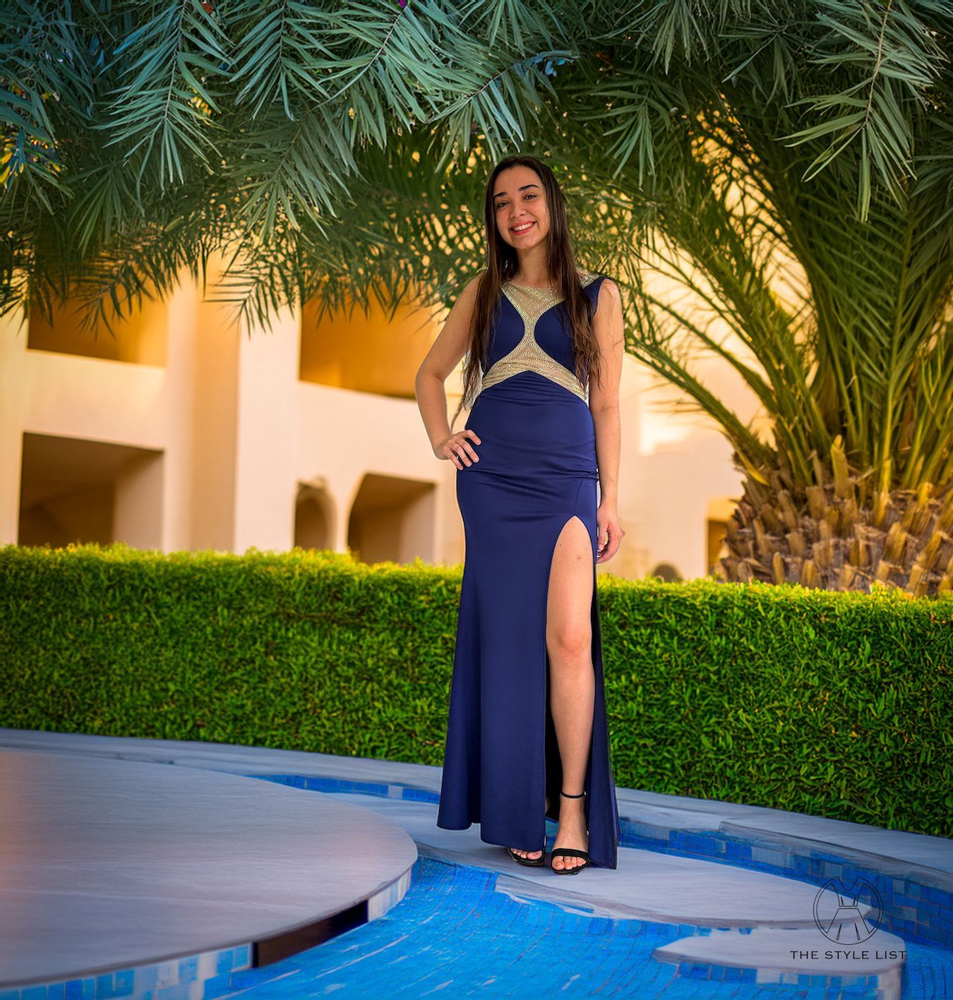 A woman in a blue dress is standing next to a pool.