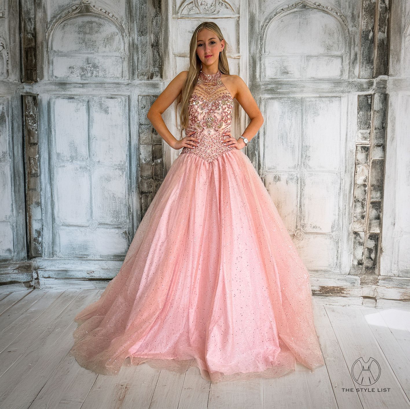 A woman in a pink ball gown is standing in front of a white wall.