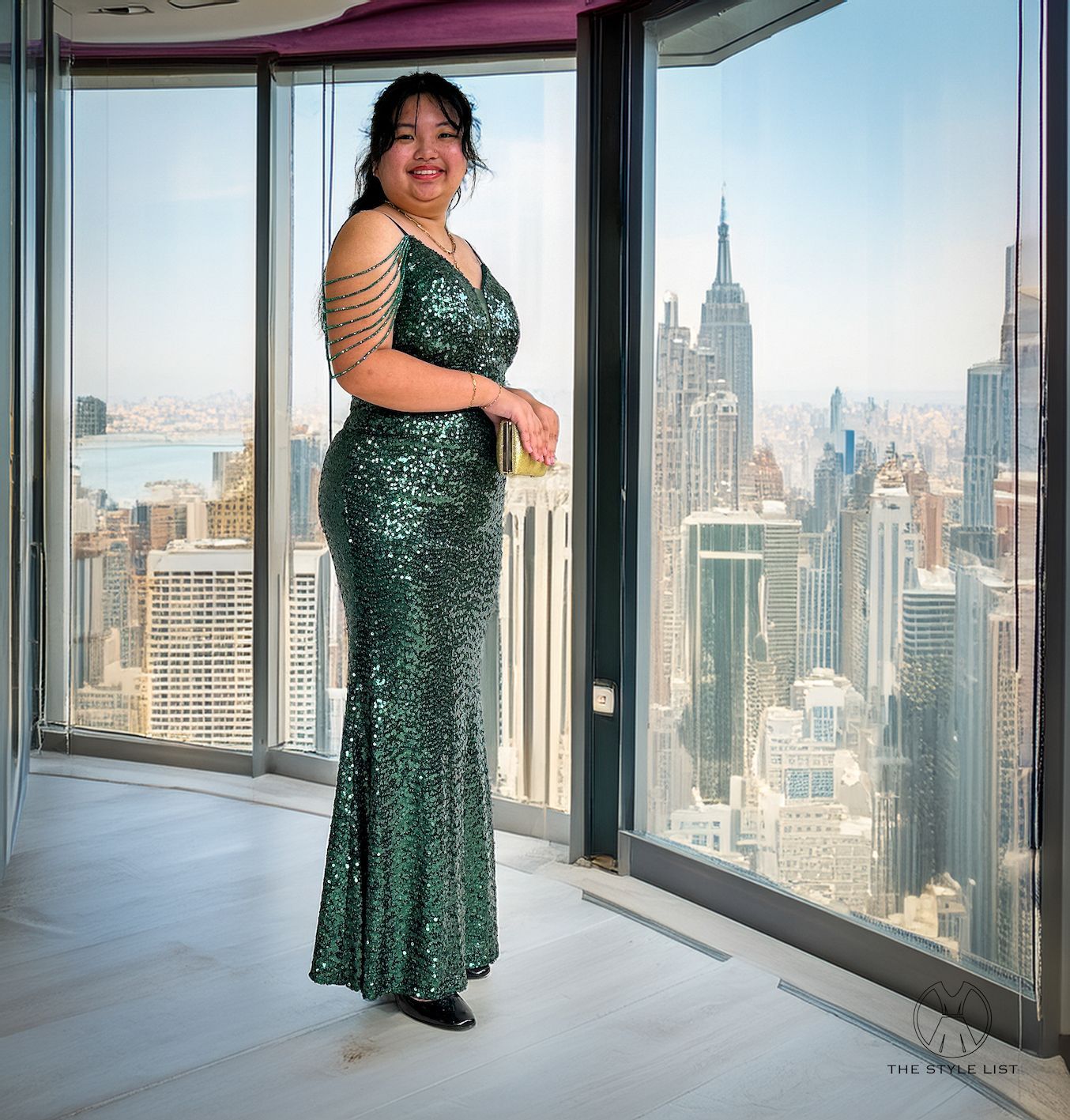 A woman in a green dress stands in front of a window overlooking a city