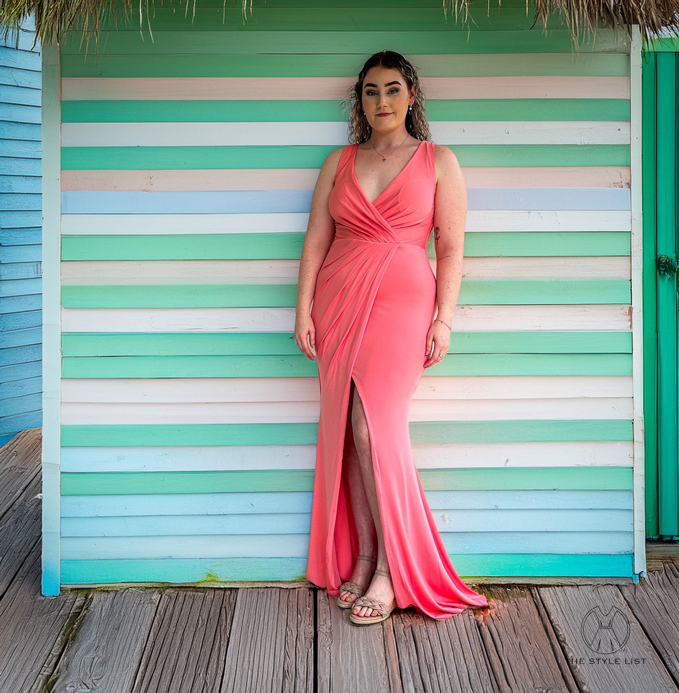 A woman in a pink dress is standing in front of a wooden wall.