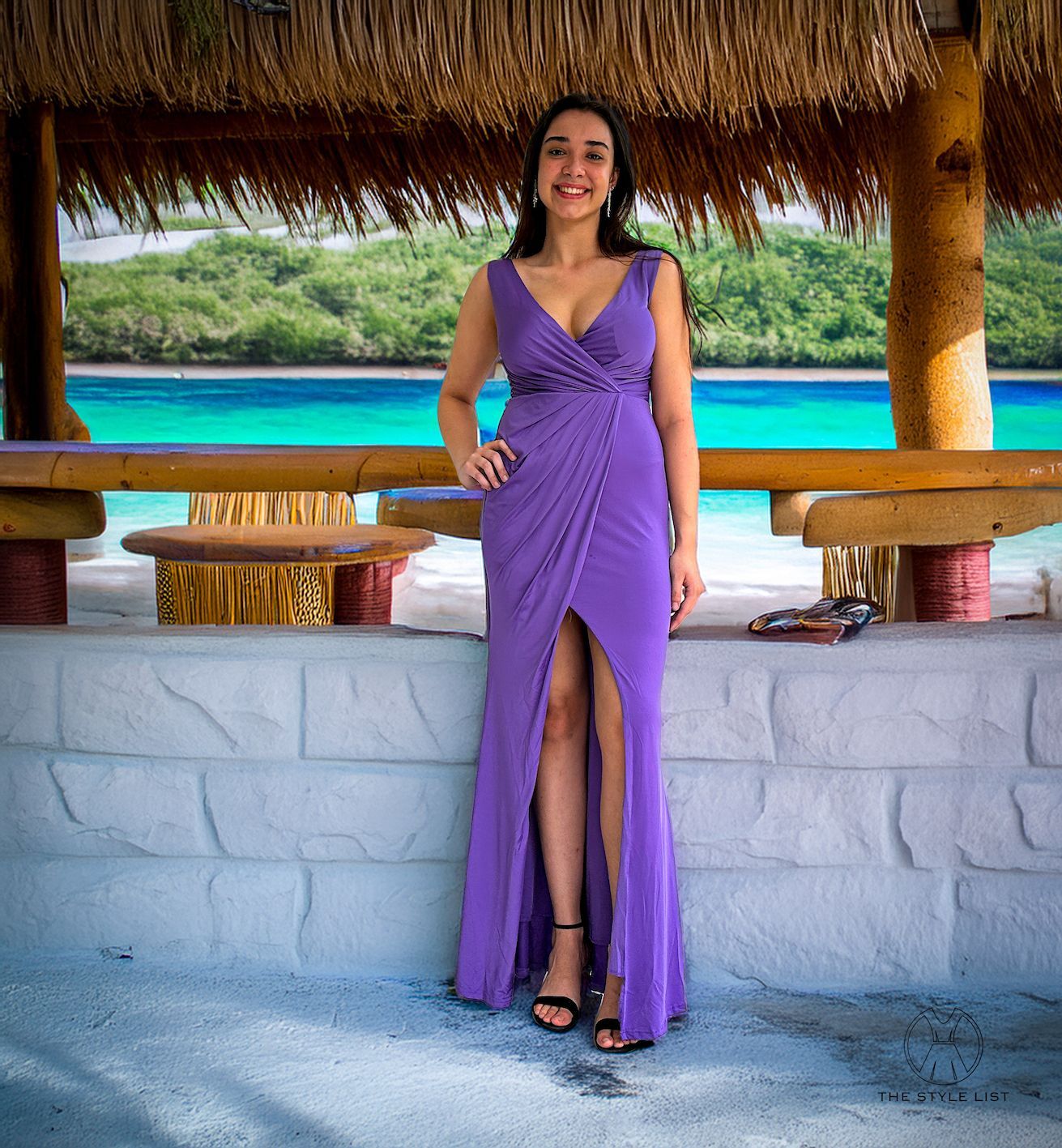 A woman in a purple dress is standing next to a brick wall