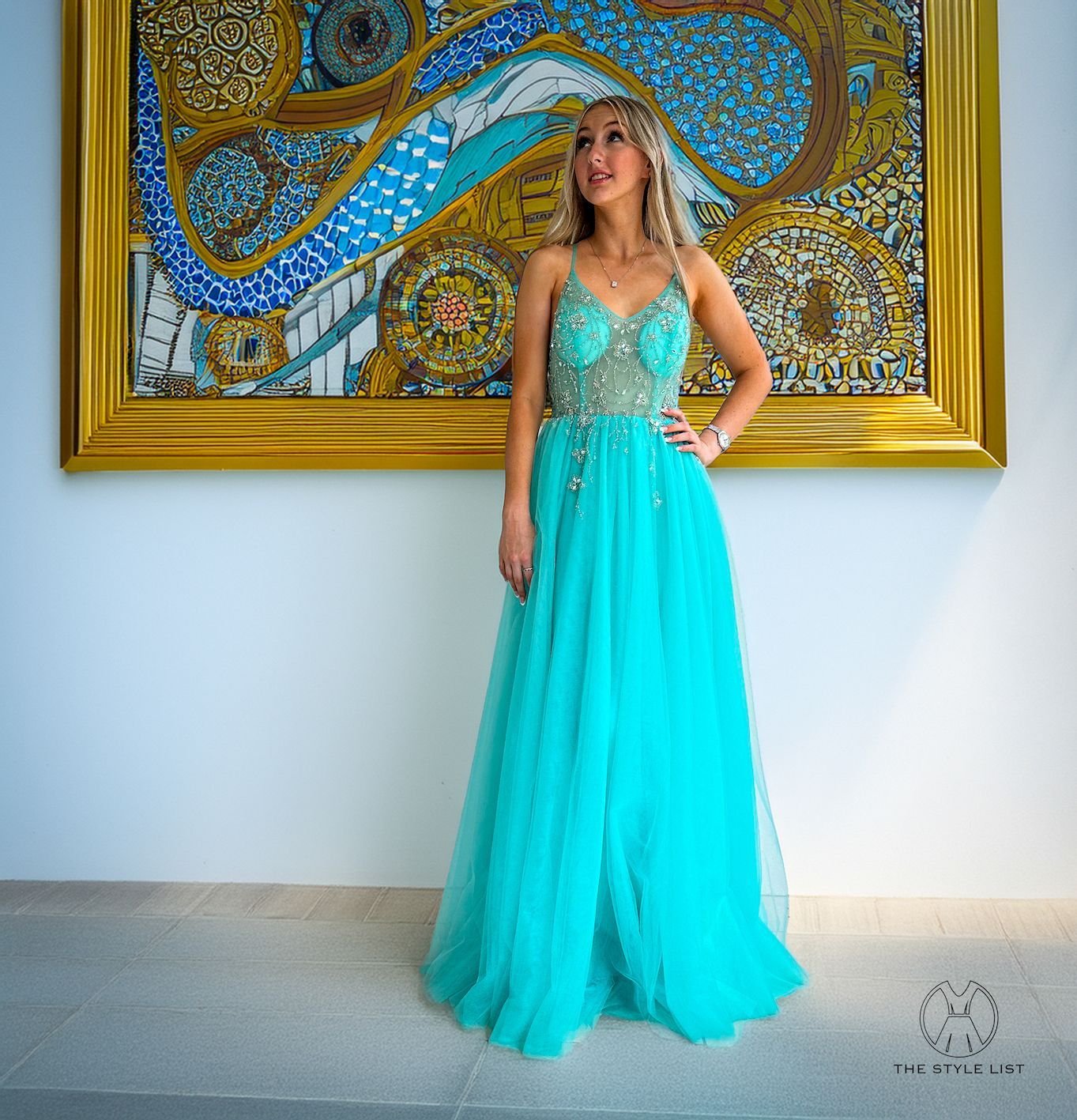 A woman in a turquoise dress is standing in front of a painting.