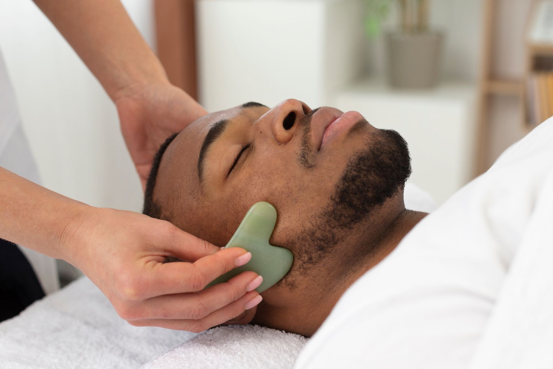 A man is getting a gua sha massage on his face at a spa.