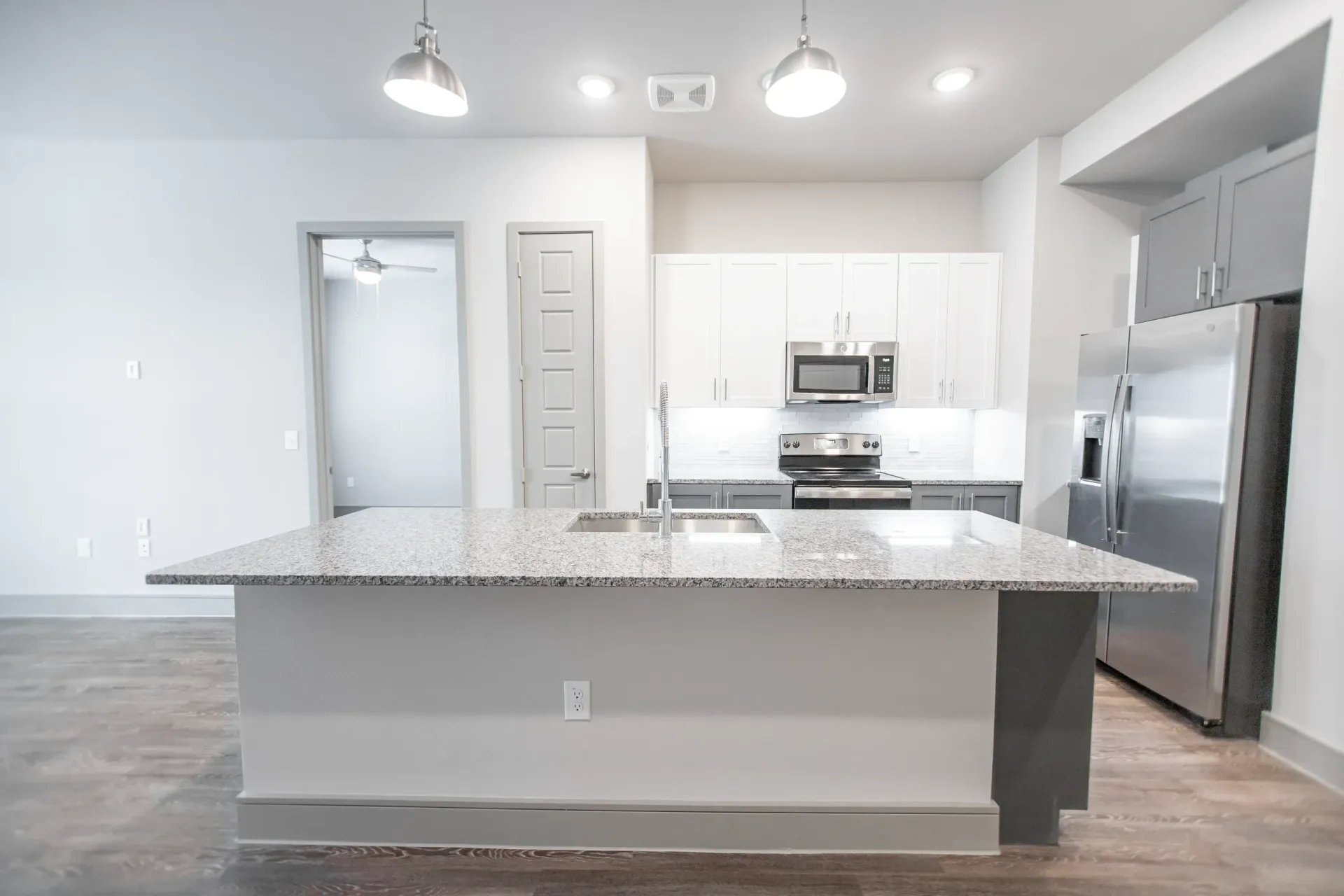 Open-concept apartment kitchen with granite island, stainless steel fridge, microwave, and white cabinetry.