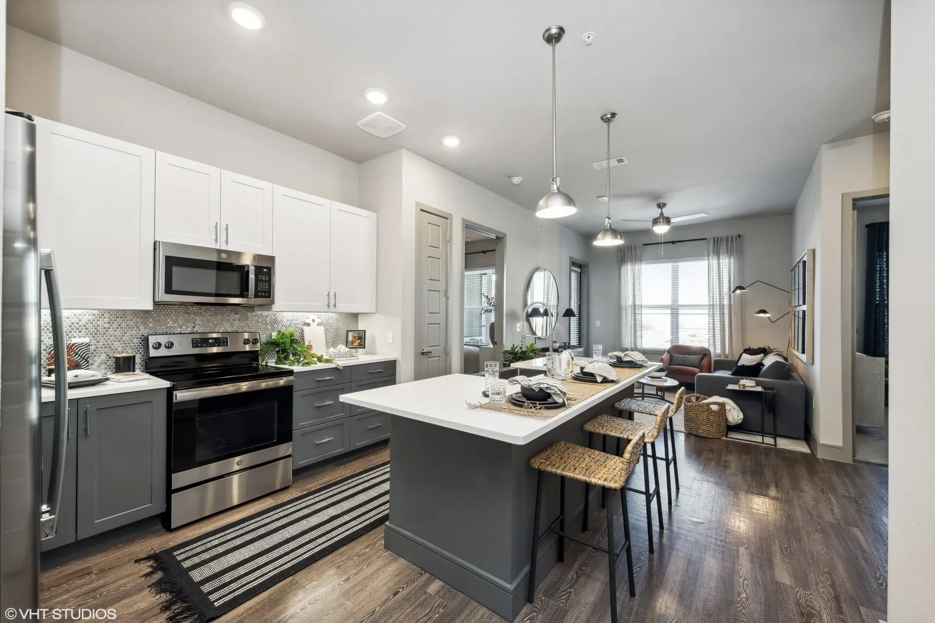 Open-plan kitchen with white upper cabinets, gray lower cabinets, stainless steel appliances, and a large island
