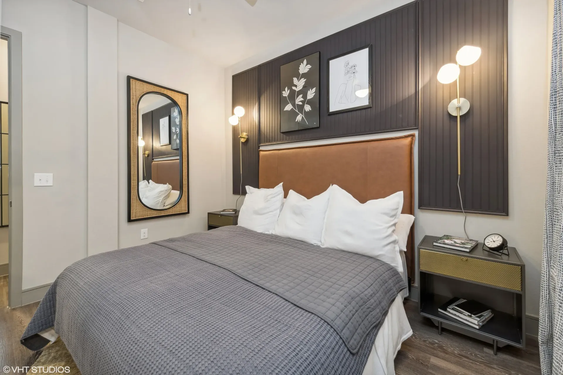 Modern apartment bedroom with a padded brown headboard, gray quilt, and two nightstands.