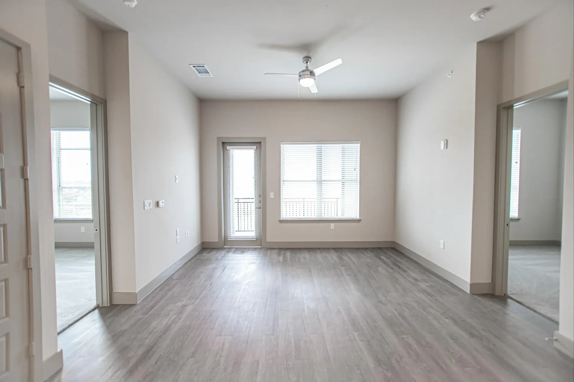 Empty living area with a balcony door, large window, and gray laminate flooring.