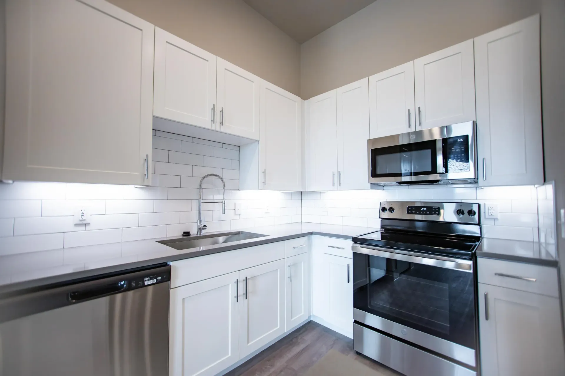 Modern white kitchen with stainless steel appliances, subway tile backsplash, and a stainless sink.
