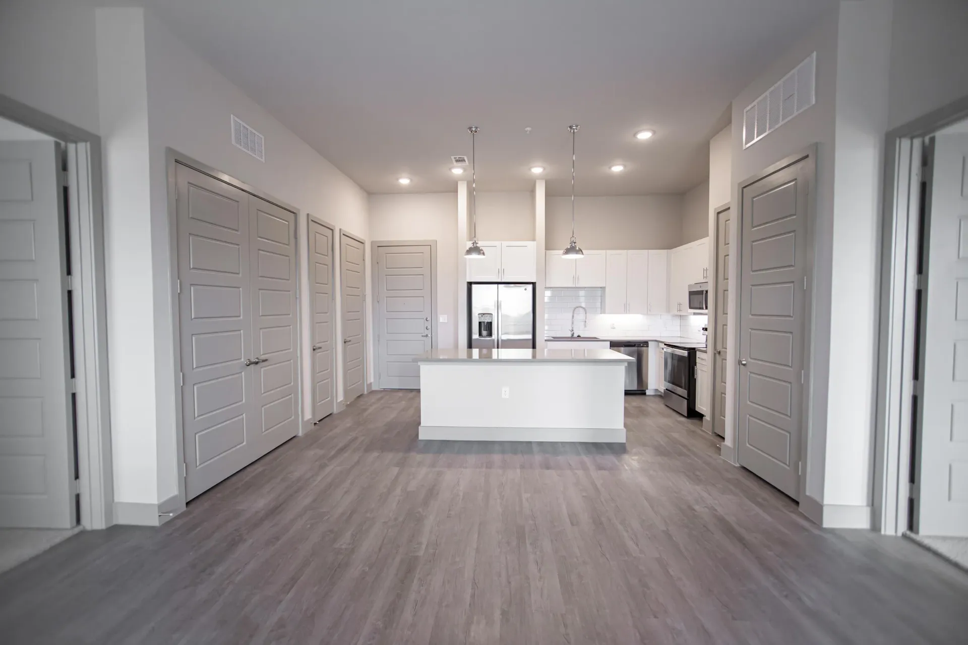 Open-concept kitchen in a modern apartment with white cabinets, island, and stainless steel appliances.