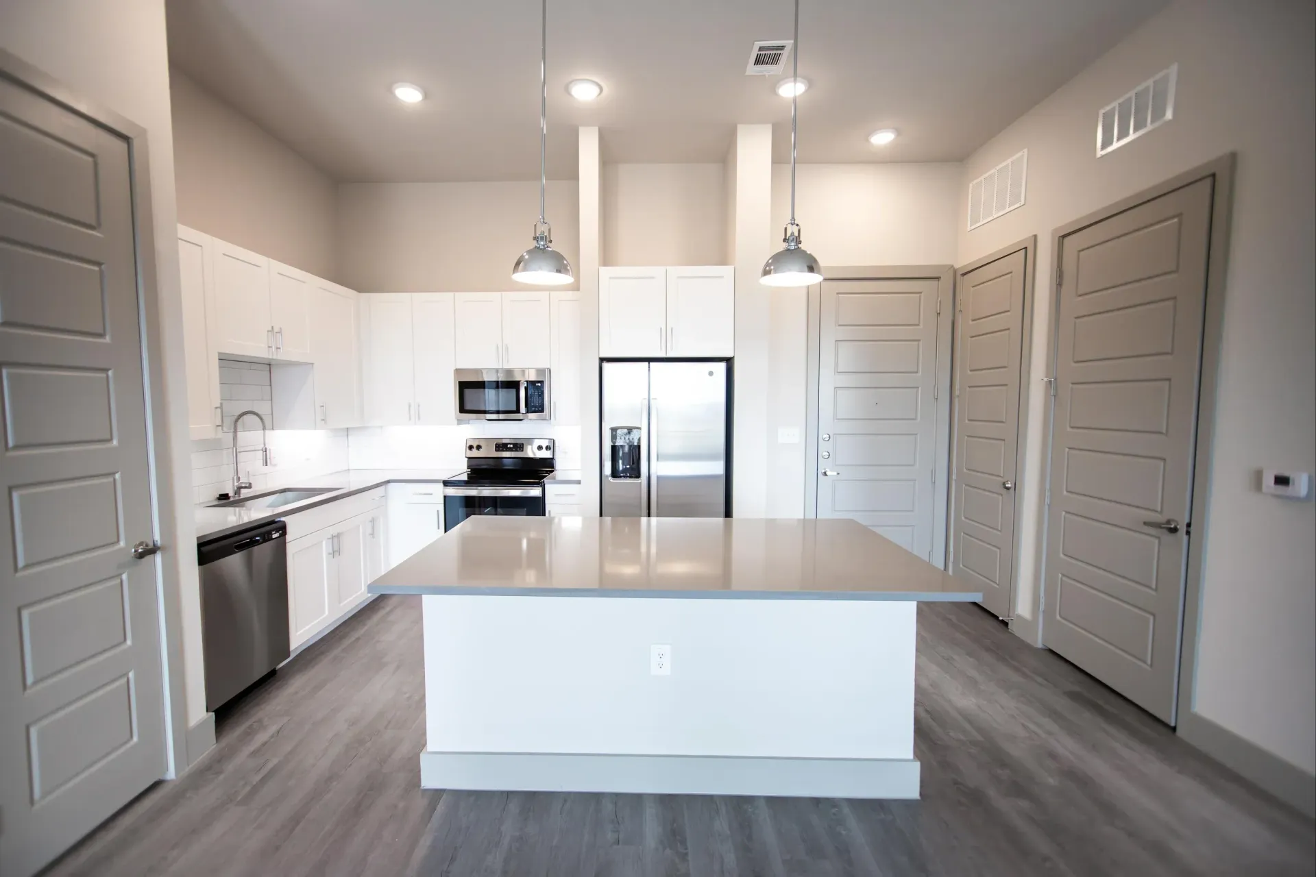 Modern apartment kitchen with white cabinets, a large island, and stainless-steel appliances.