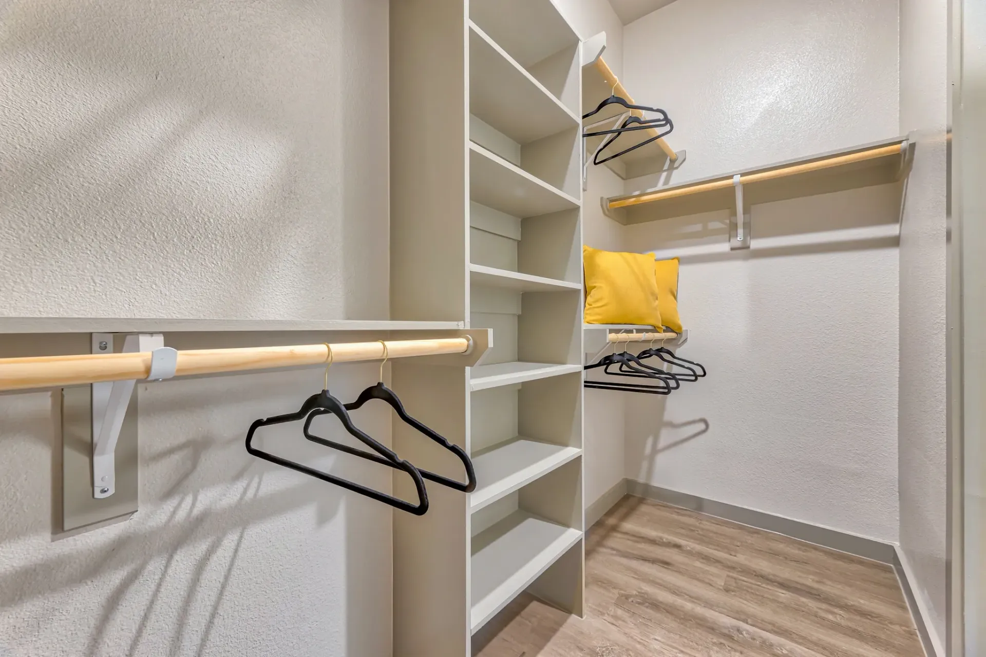 Walk-in closet with white shelves, hanging rods, and hangers on a wood floor.