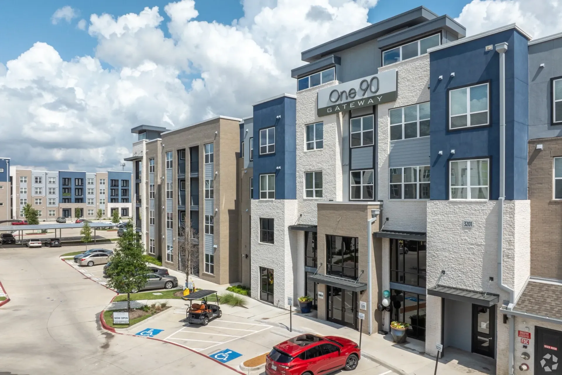 Exterior view of a modern apartment community with signage and parking.