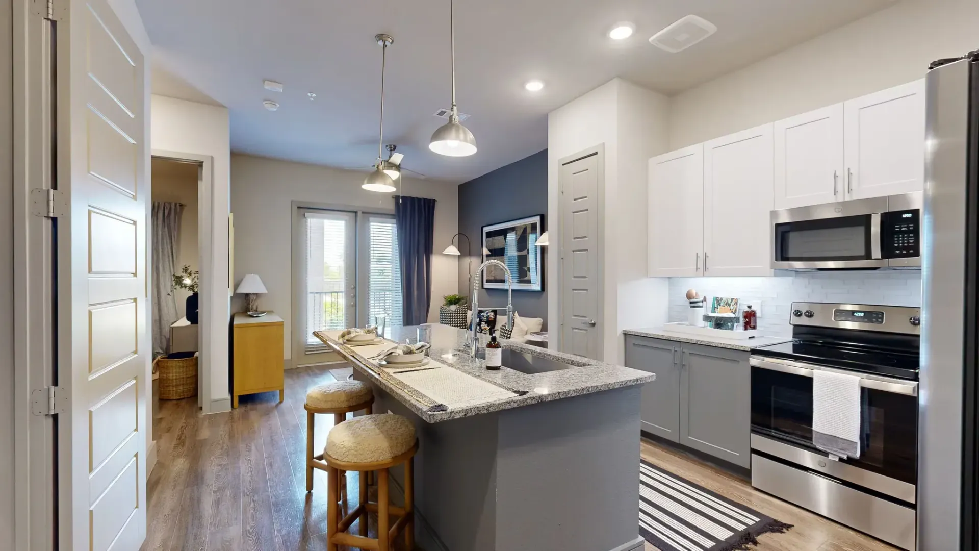 Open-concept kitchen with granite island, stainless steel appliances, and two bar stools.