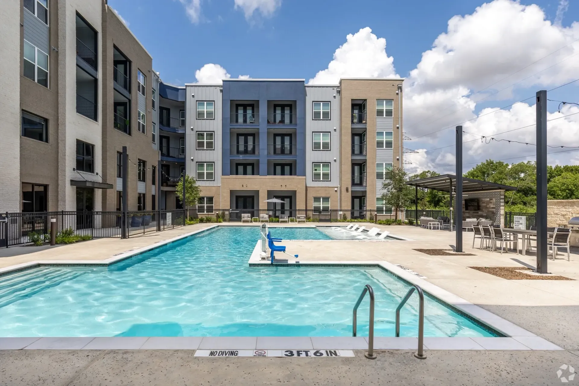 Outdoor pool at a multifamily property with lounge chairs and a shaded seating area against a modern building backdrop.