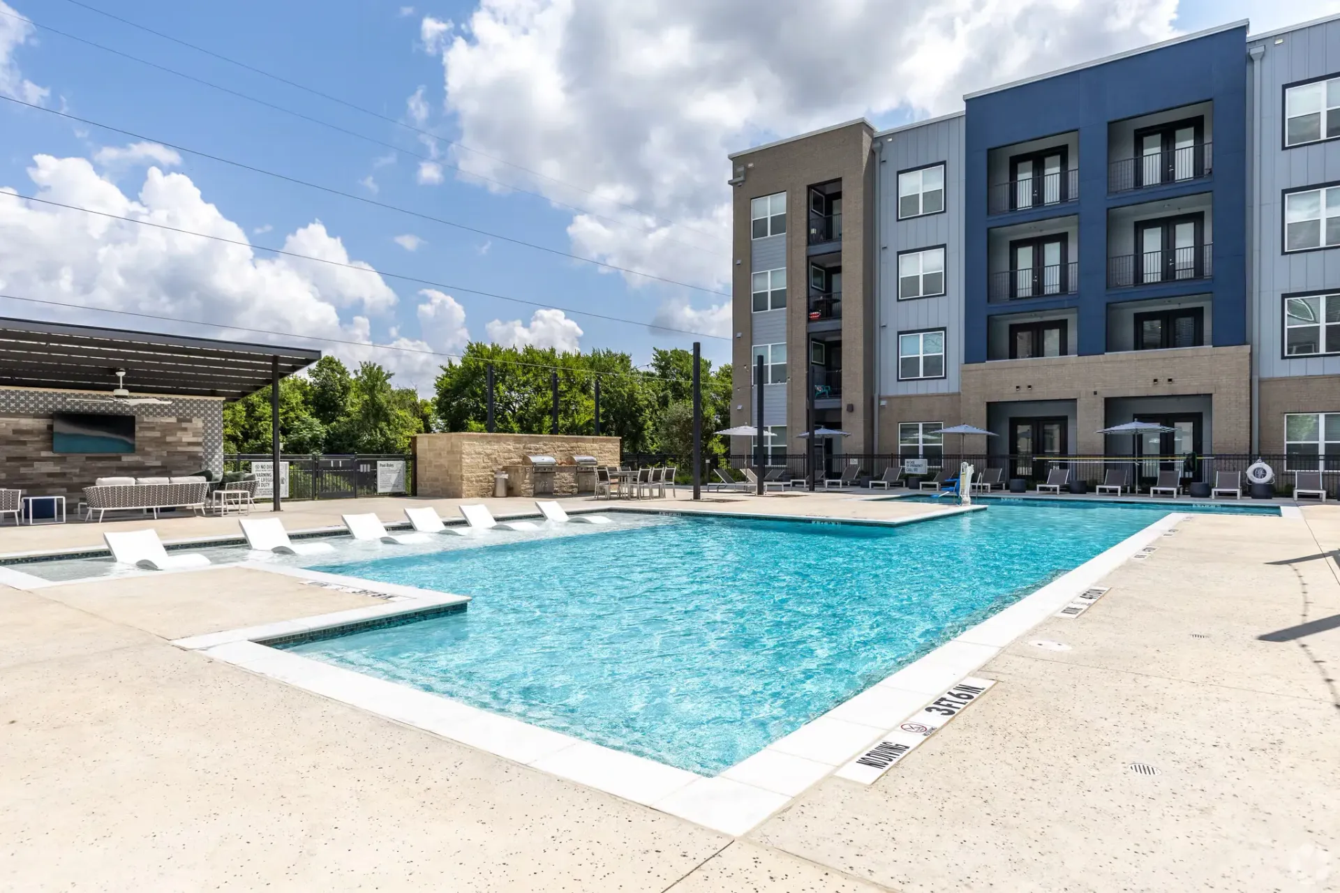 Outdoor community pool with lounge chairs and a modern apartment building in the background.