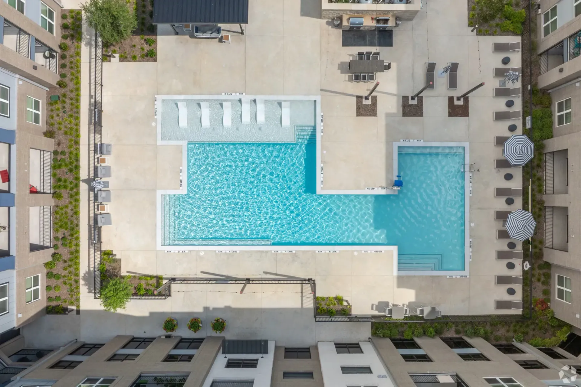 Aerial view of a multi-building apartment courtyard with a large central pool and lounge areas.