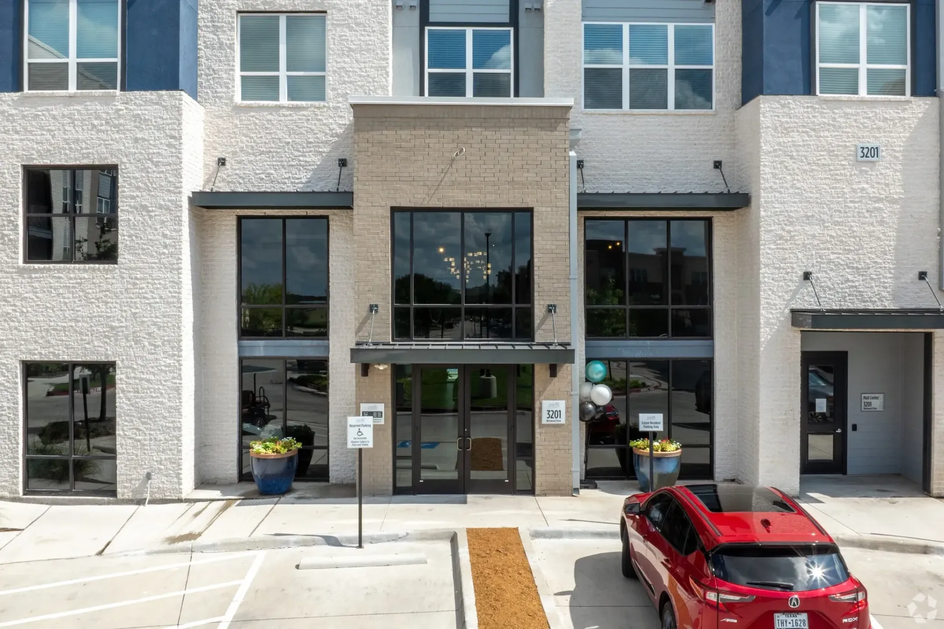 Front exterior of a modern apartment building with glass entry doors and large windows.