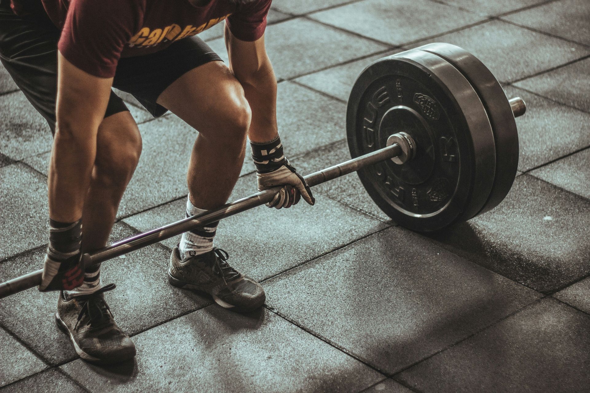 Person deadlifting a heavy barbell on a gym floor, with close-up view of legs and hands.