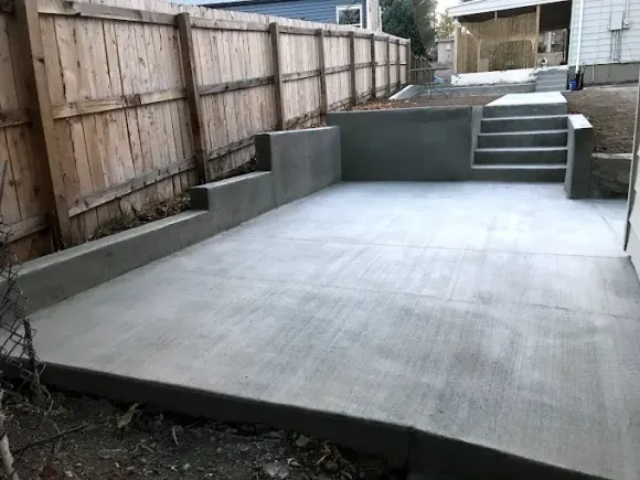 A concrete patio with stairs and a wooden fence in the background.