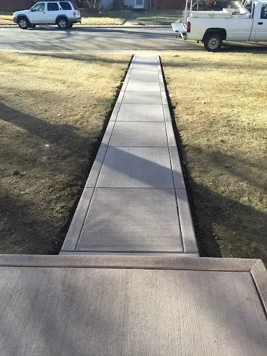 A white truck is parked on the side of the road next to a concrete walkway.