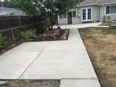 A concrete walkway leading to a house with a fence in the background.