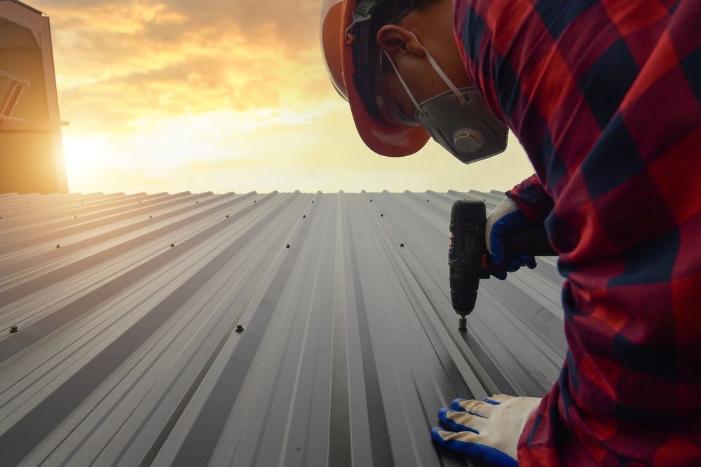 A man is using a drill to fix a metal roof.