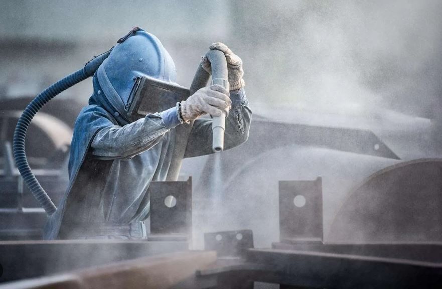 A sandblaster professional wearing protective gear cleaning an industrial beam