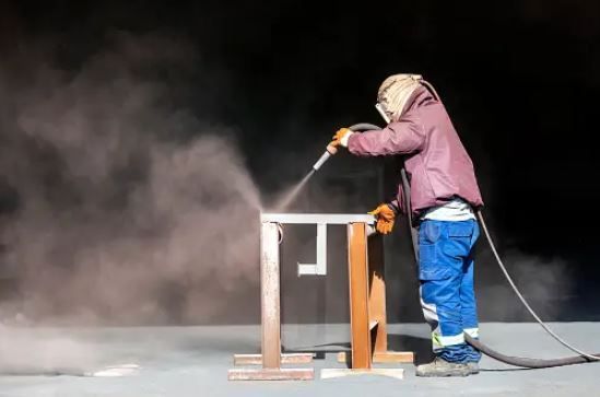 A man using a sandblaster to remove the varnish from a table