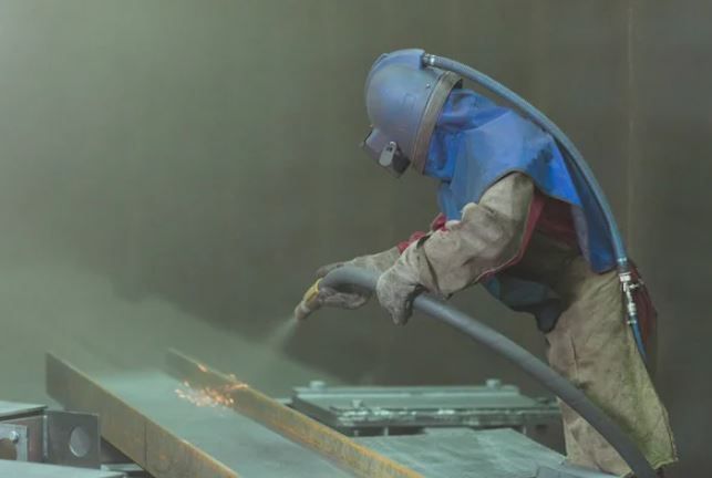 A sandblaster removing rust from a construction beam
