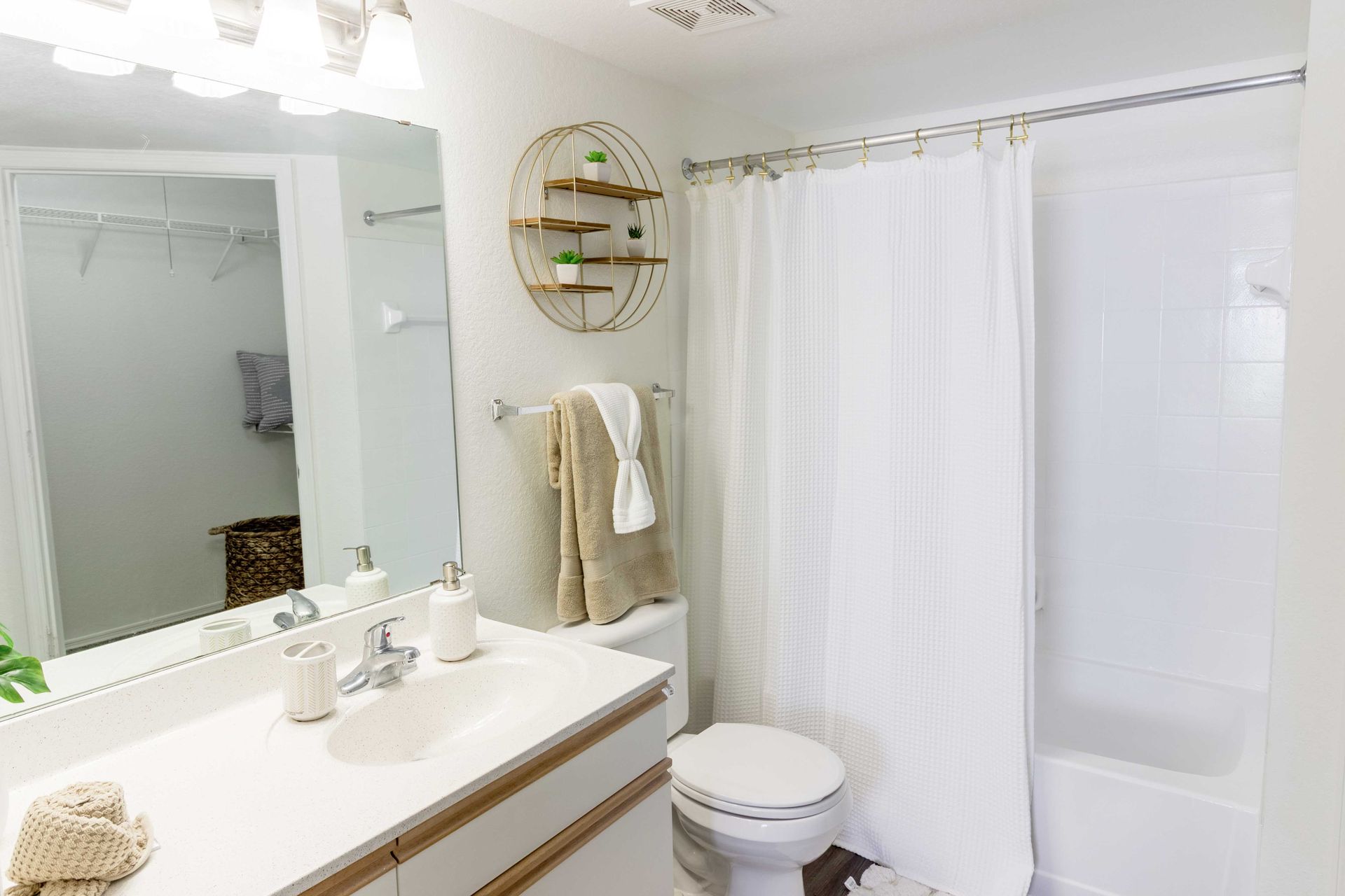 Bathroom with white decor: sink, toilet, bathtub, mirror, and a shelf with plants at The Point at Naples in Naples, FL.