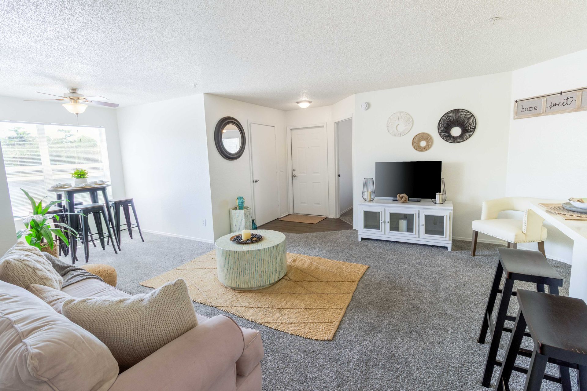 Living room with sofa, TV, and rug; neutral colors at The Point at Naples in Naples, FL.