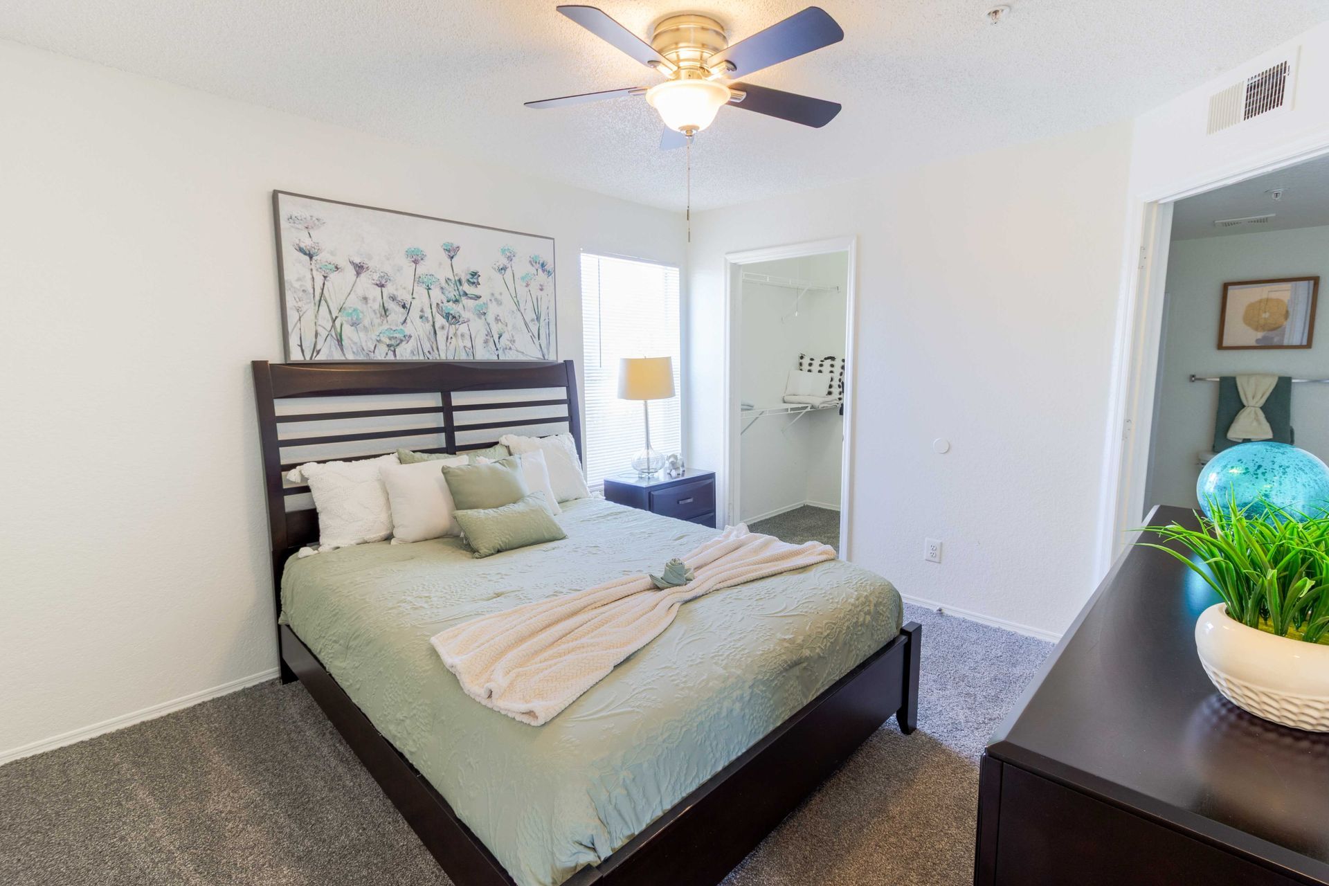 Bedroom with bed, nightstand, art, and open doorway to bathroom. Light green and white decor at The Point at Naples in Naples, FL.