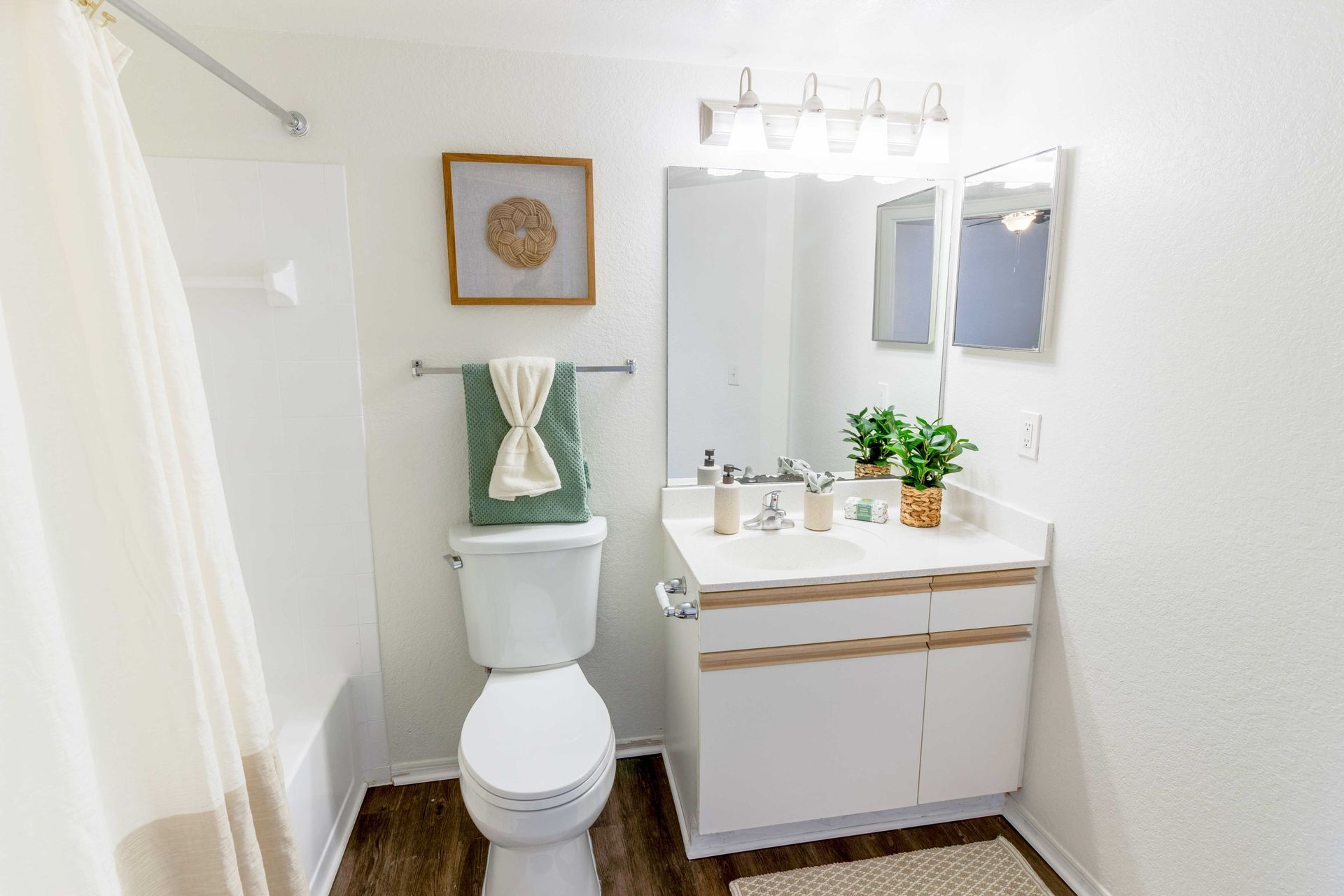 Bathroom with white walls, vanity, and shower. Features a toilet, towel rack, and woven artwork at The Point at Naples in Naples, FL.