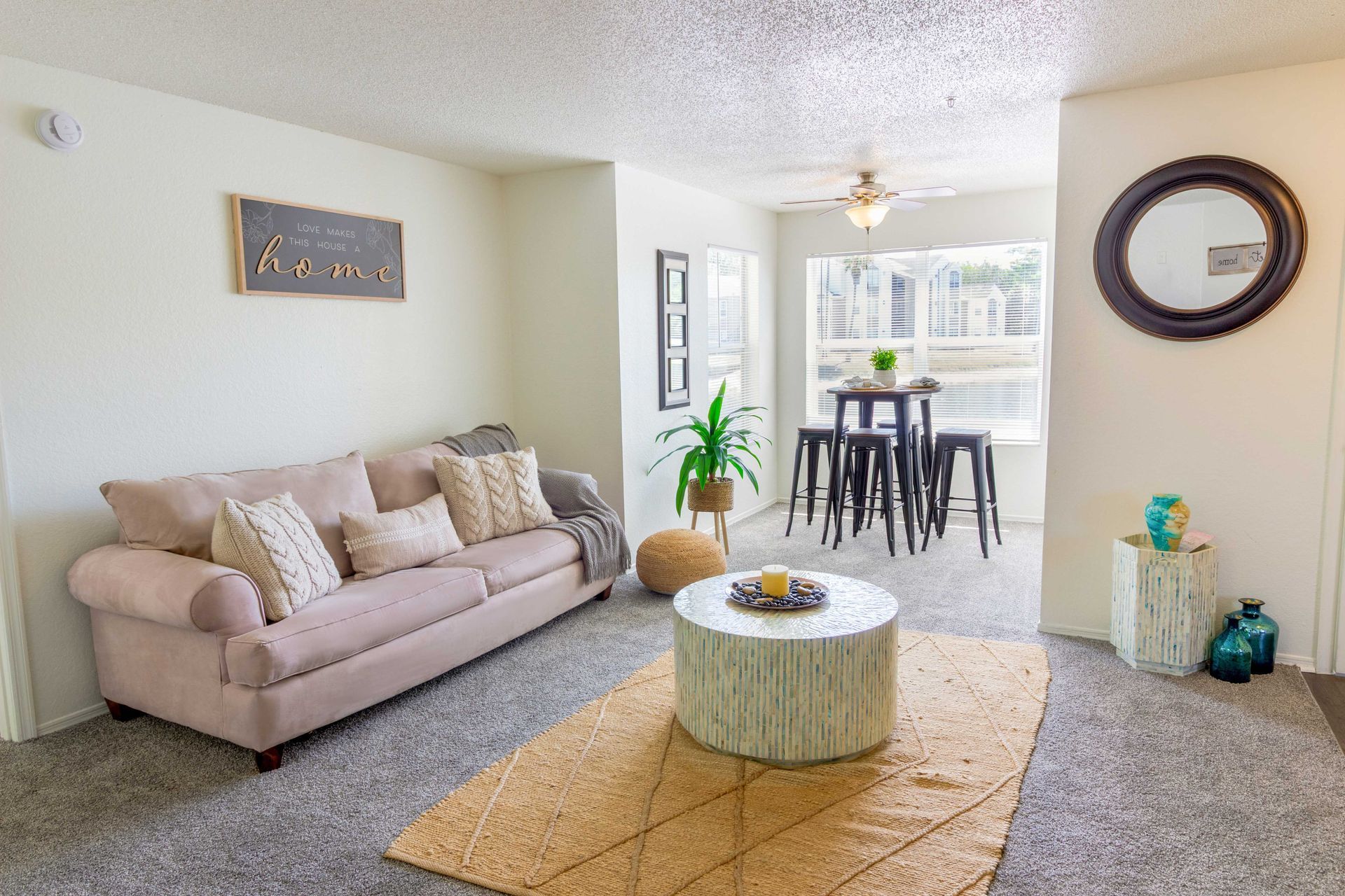 Living room with sofa, round coffee table, and dining table by a window at The Point at Naples in Naples, FL.