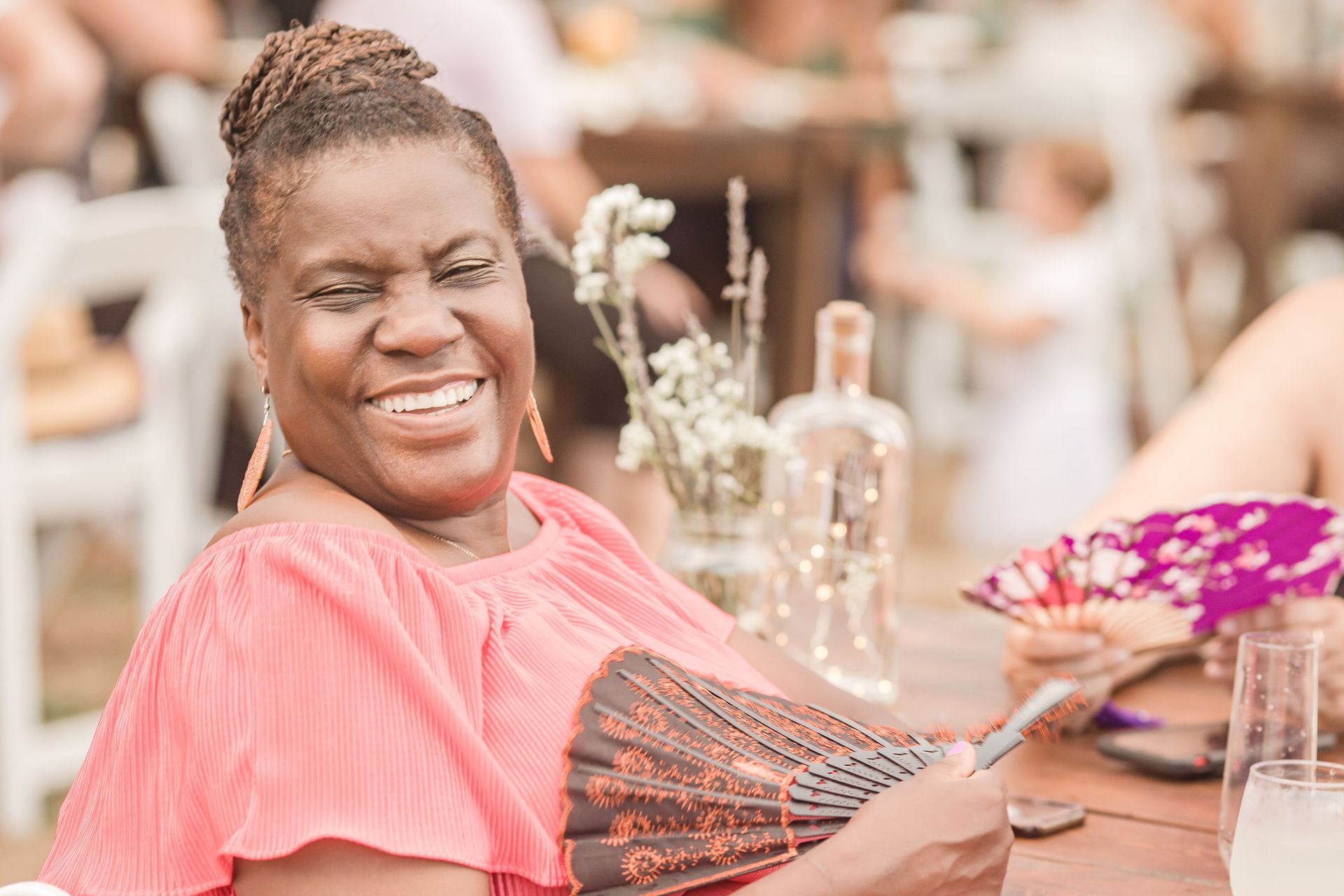 A woman is sitting at a table holding a fan and smiling.