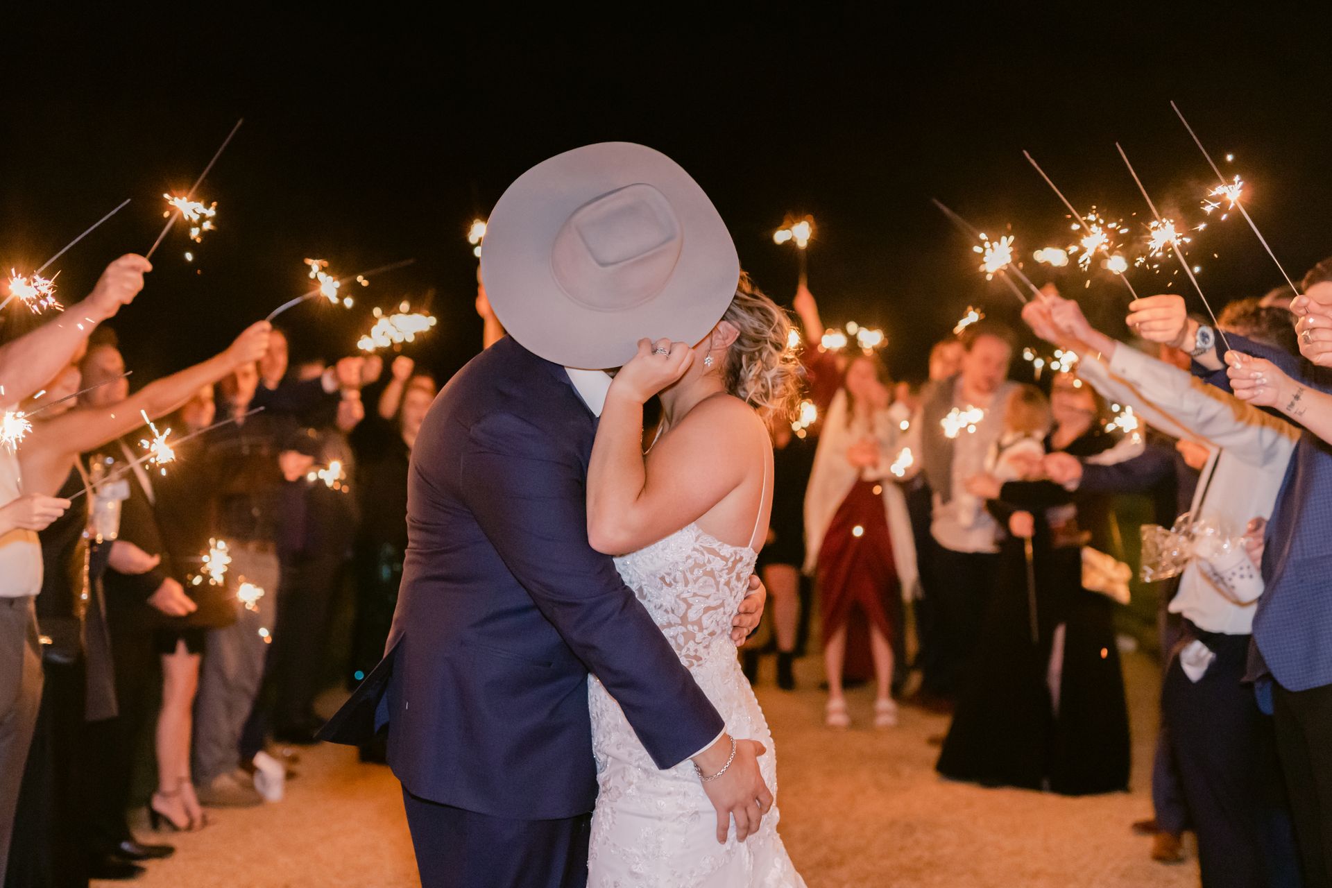 A bride and groom kissing in front of a crowd of people holding sparklers.