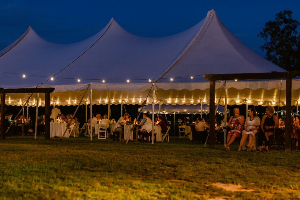 A group of people are sitting at tables under a tent at night.