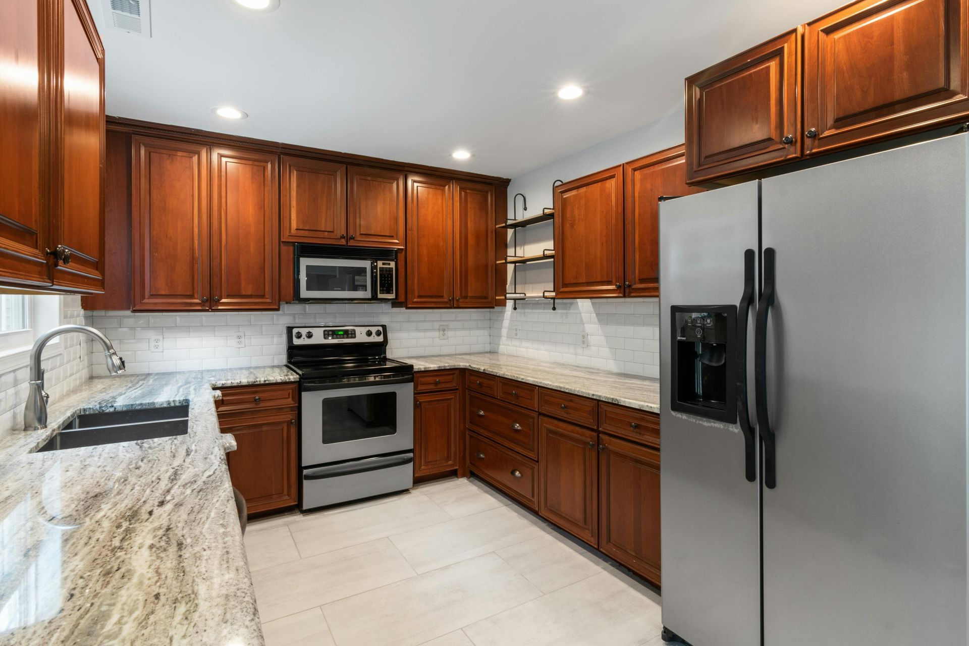 A kitchen with warm wood cabinets, granite countertops, stainless steel appliances, and a tiled floor.